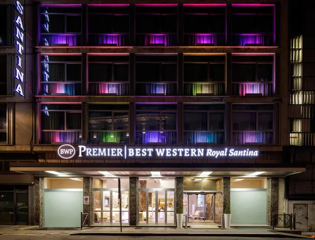 Night view of the illuminated facade and entrance of the Premier Best Western Royal Santina hotel, with its name lit on the canopy.