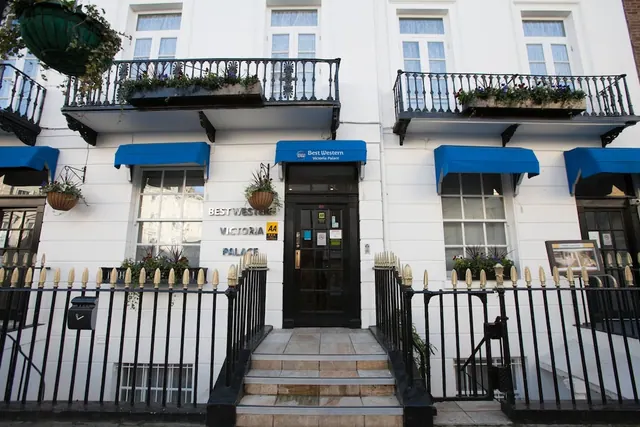 The white front of the Best Western Victoria Palace hotel, with blue awnings, black railings, flower boxes and steps leading up to the entrance door.