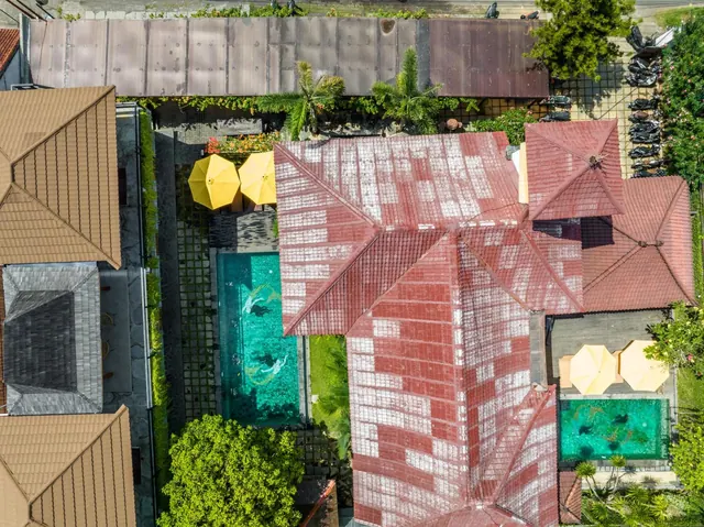 Aerial view of a property with red tiled roofs, two swimming pools, yellow umbrellas and palm trees.