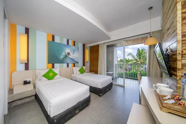 A bedroom with two twin beds against a striped wall with a surfing artwork, a wall-mounted TV, and a sliding door opening onto a balcony with palm trees beyond.