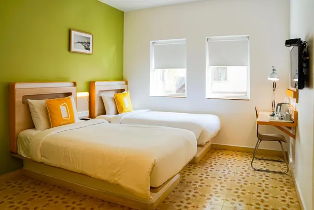 A bright twin bedroom has two beds, a desk, a wall-mounted television and patterned floor tiles.