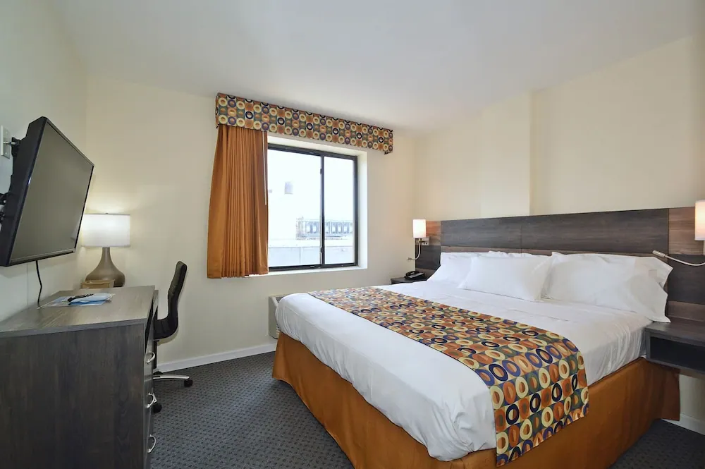 A hotel bedroom with a king bed, wall-mounted television, desk with chair, and a window looking out onto a neighbouring building.