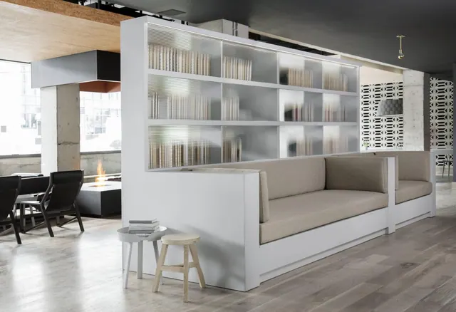 A lounge seating area with a white built-in sofa, frosted glass shelving, dark chairs and a fire feature in the background.