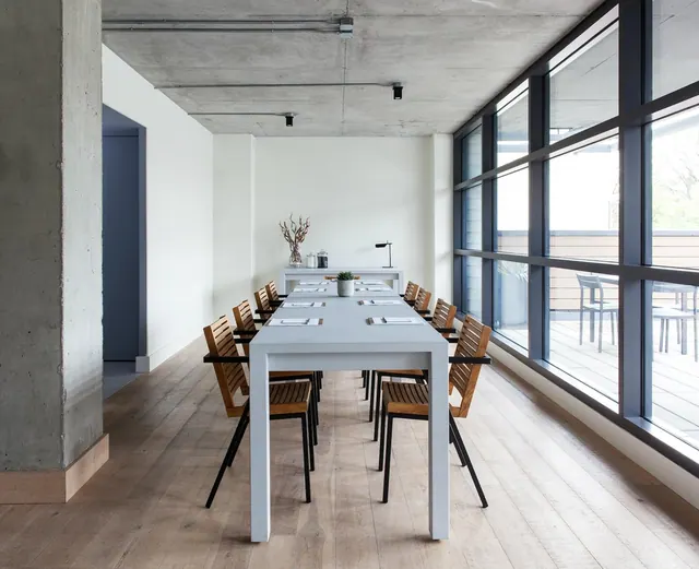 A long dining room with a grey table set with place settings and wooden chairs, with floor-to-ceiling windows along one side overlooking an outdoor deck.