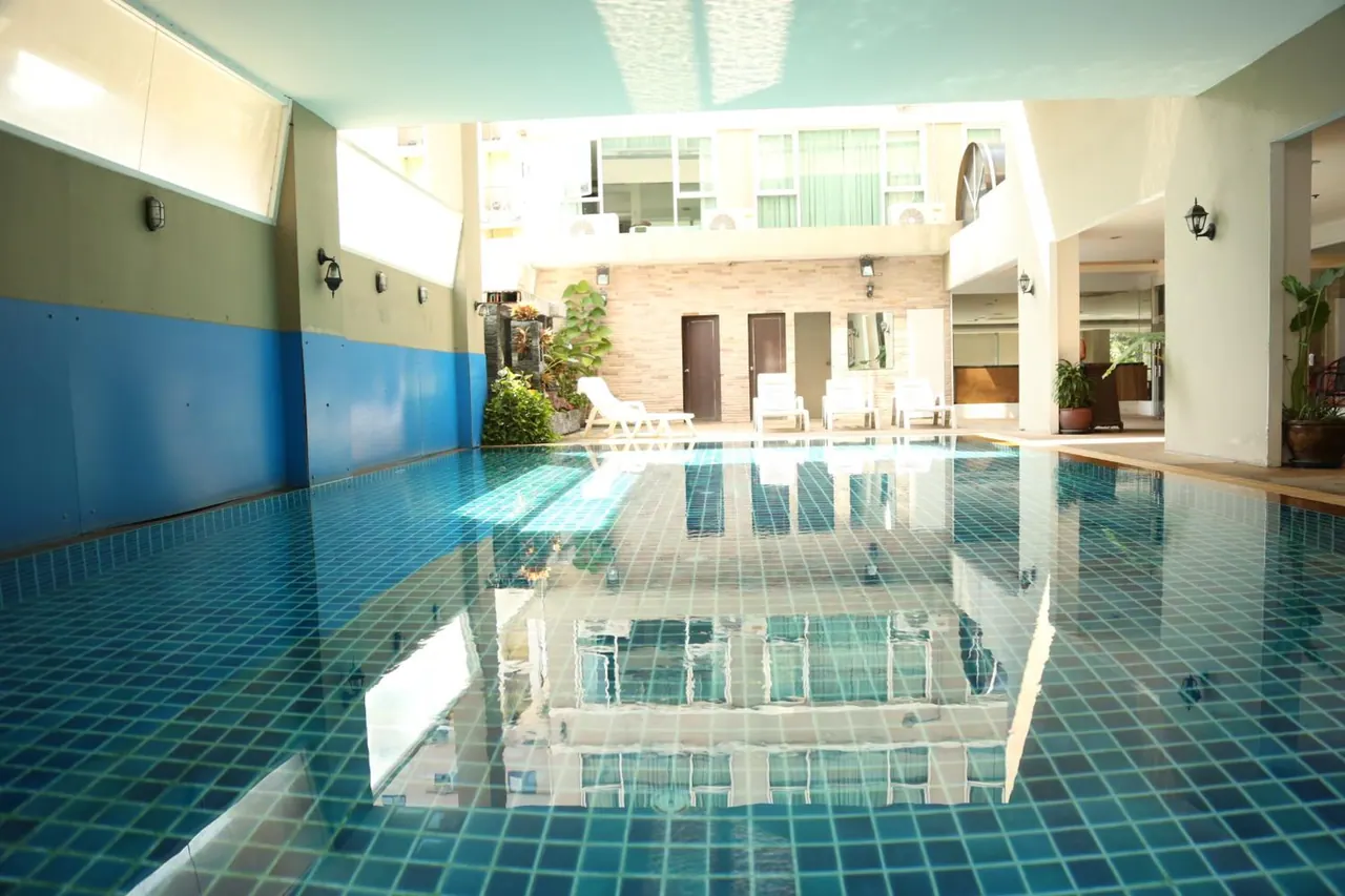 An indoor swimming pool with blue tiles, white sun loungers at the far end and a reflection of the building in the water.