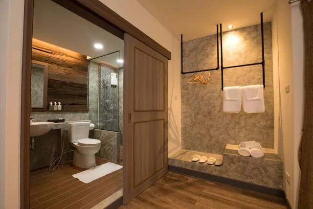 A bathroom with a toilet, wash basin, glass-enclosed shower and white towels on a rail, seen through a wooden sliding door.