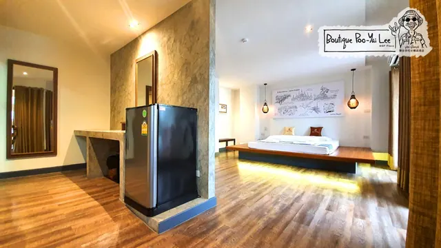A bedroom with a platform bed, a small black fridge beside a stone accent wall, and a wall mural, with a logo overlay in the top right corner.