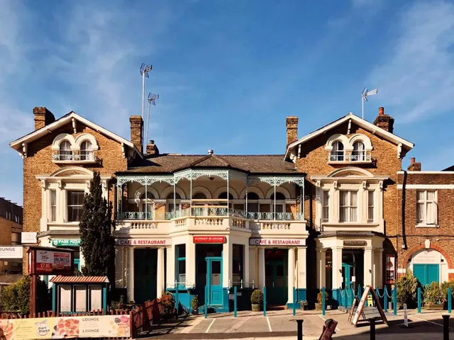 The front of a Victorian brick building with a cafe and restaurant frontage, teal doors, a pizza banner along the pavement and bollards in the street.