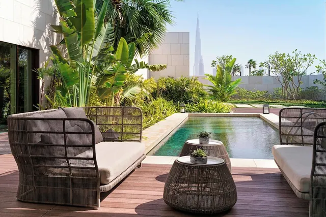 A furnished outdoor terrace with wicker seating and side tables beside a small pool, with the Burj Khalifa visible in the background.
