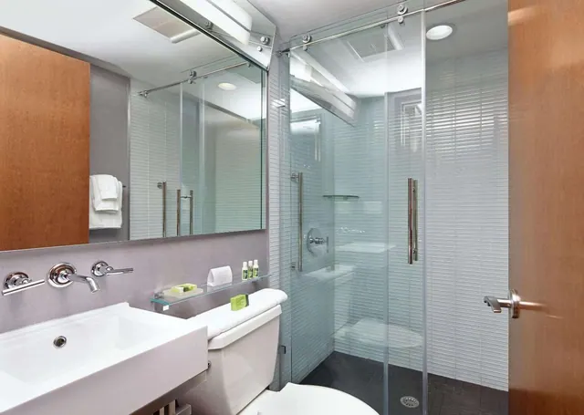 A bathroom with a glass-enclosed walk-in shower, a wall-mounted faucet above a white sink, and a toilet with a folded towel on the tank.