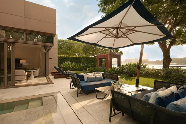 A terrace with outdoor sofas and a large cantilever umbrella beside a small plunge pool, with a garden and a river beyond.