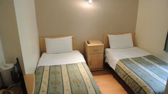 Two single beds with striped green covers sit either side of a light wood bedside cabinet in a small room.
