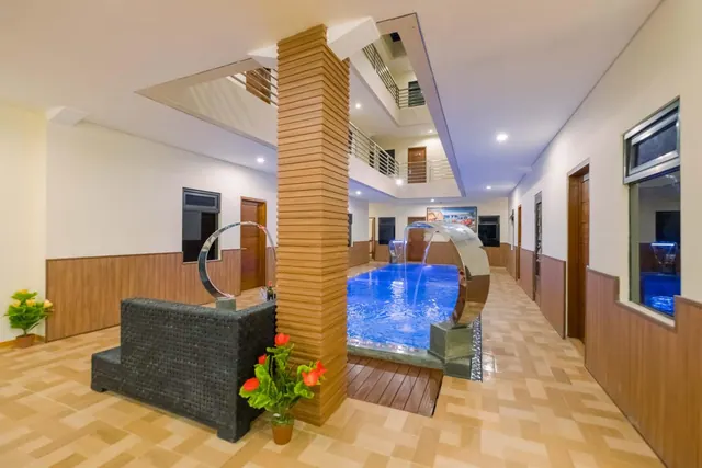 An indoor swimming pool with stainless steel arc water features sits beside a dark wicker sofa and a wood-slatted pillar, under a multi-level atrium with balconies.