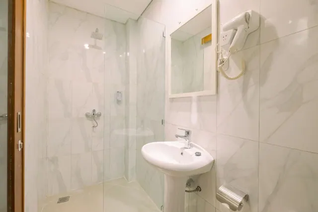 A bathroom with marble-look tiled walls, a glass-enclosed walk-in shower, a pedestal sink, a mirror and a wall-mounted hair dryer.