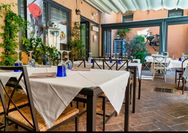 An outdoor courtyard dining area with white-clothed tables, upturned blue wine glasses, rush-seat chairs, climbing plants and a bicycle hanging on the wall.
