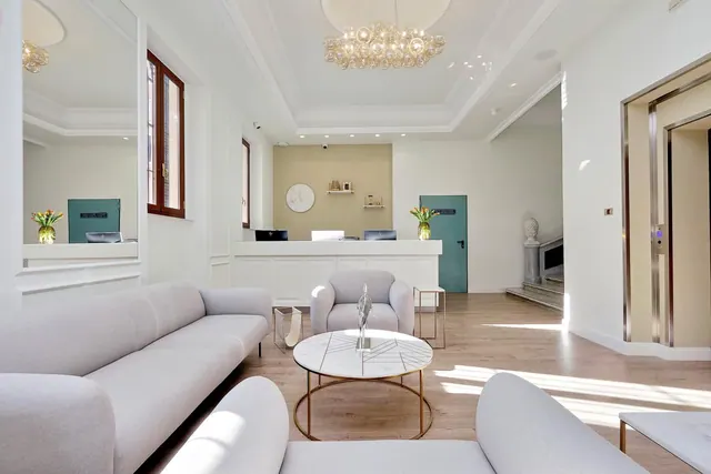 A lobby with white sofas, a round marble coffee table, a reception desk and a lift on the right.