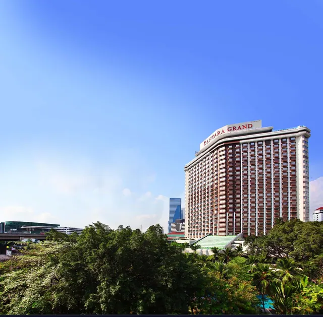 Exterior view of the Centara Grand hotel tower under a clear blue sky, with trees in the foreground.