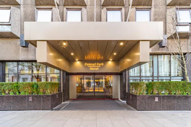 The front entrance of Central Park Hotel, with a covered canopy over glass doors and hedge planters on either side.