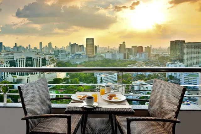 A breakfast table with plates, cups and juice sits on a balcony overlooking a city skyline at sunset.