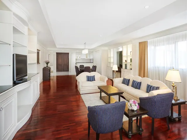 A living room with a cream sofa and loveseat, blue striped armchairs, a flat-screen television on built-in white cabinets, and dark wood flooring.