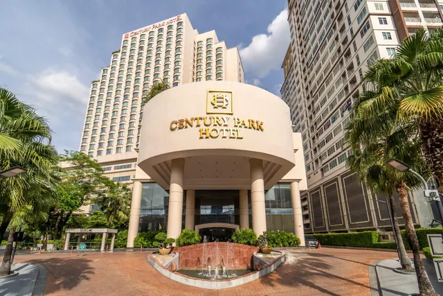 Wide-angle view of the Century Park Hotel entrance with a curved portico, a fountain in the forecourt, palm trees and tall towers behind.