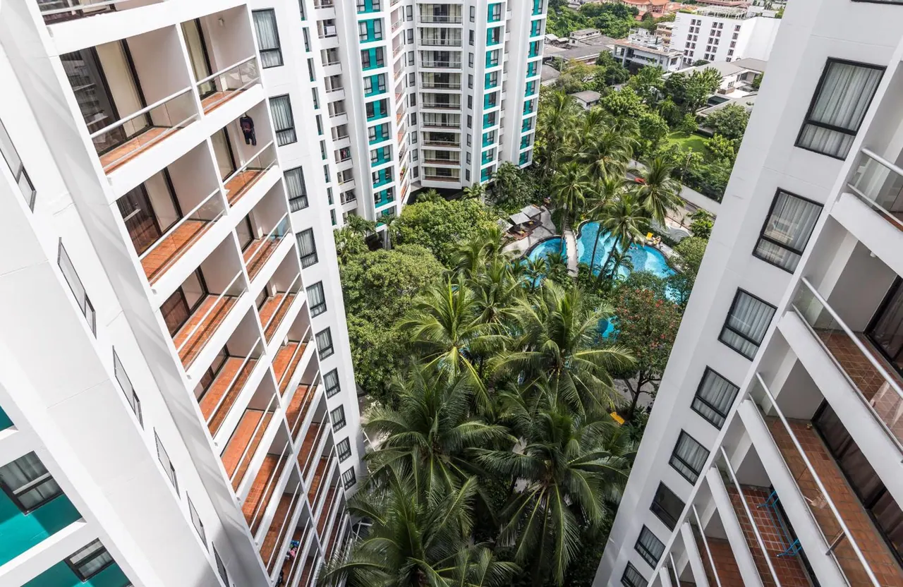 Looking down from an upper floor between two white residential towers onto a palm-lined courtyard with a swimming pool.