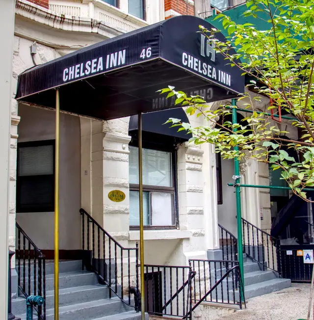 The entrance of the Chelsea Inn building, with a black awning, stone steps, iron railings and a leafy tree at the right.