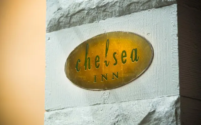 A golden oval sign with green script reading chelsea INN is mounted on a white stone wall.