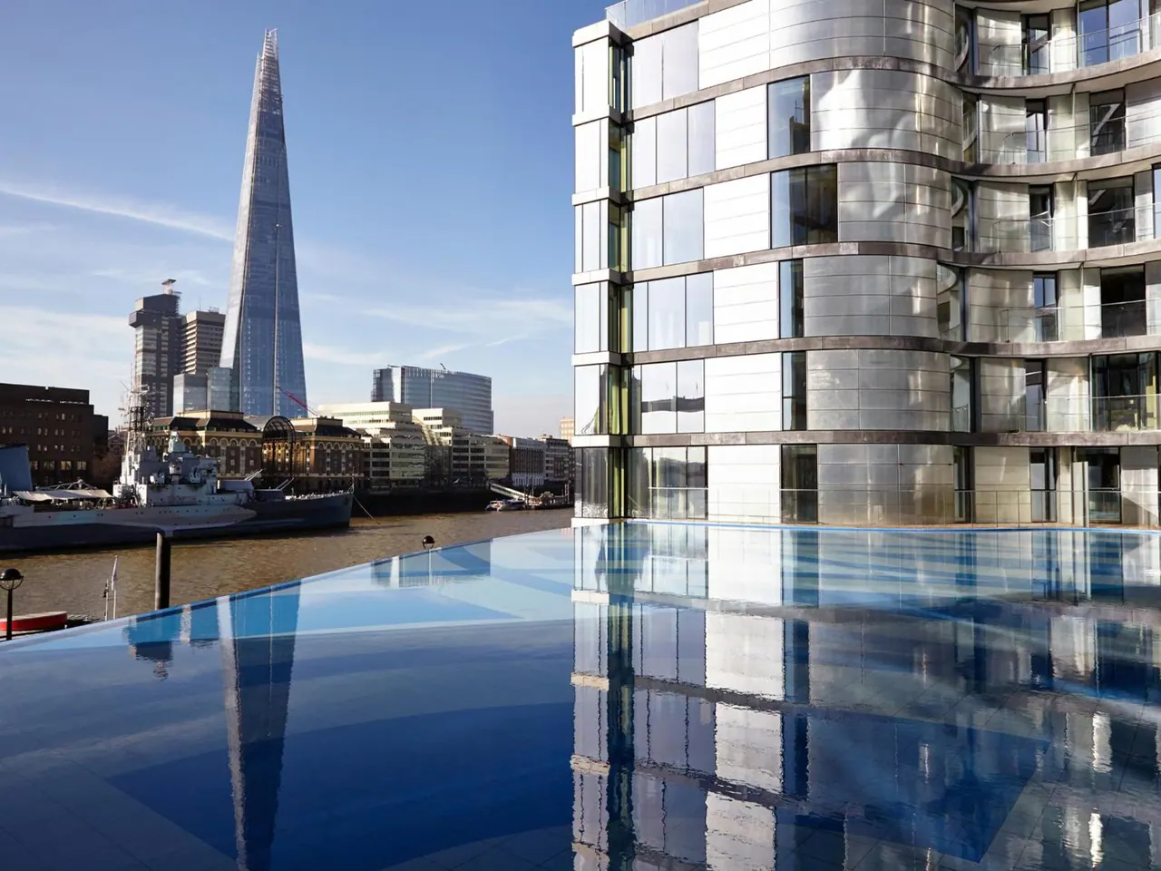 An infinity-edge pool overlooks the River Thames, with The Shard and the moored warship HMS Belfast visible beyond.