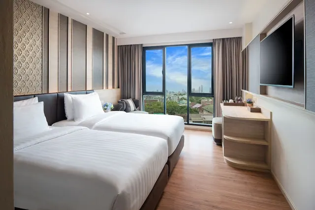 A hotel bedroom with two single beds, a wall-mounted television, and a large window overlooking the city.