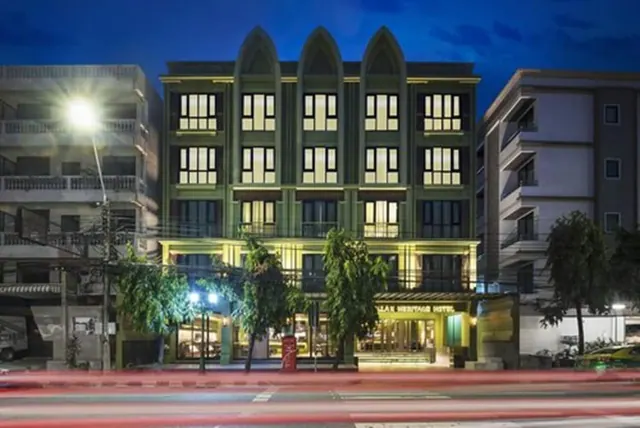 Evening exterior of a green hotel building with arched gables and lit windows, with part of its name sign visible at street level.