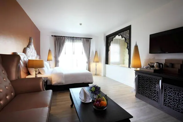 A hotel room with a double bed, a tufted leather armchair, a wall-mounted television, a carved wooden cabinet and a fruit bowl on a coffee table.
