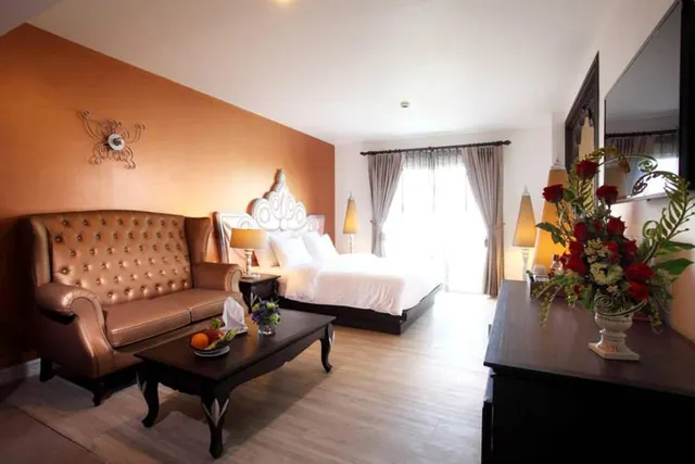 A hotel bedroom with a made bed, a tufted leather sofa, a coffee table with a fruit bowl, and a dresser holding a vase of red roses.