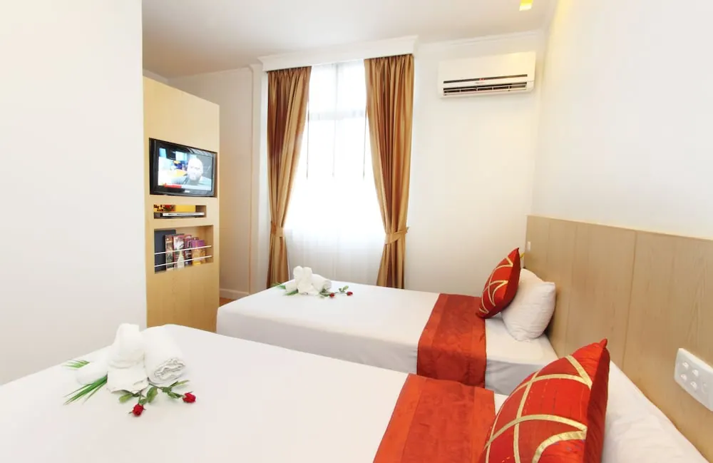 Two single beds with red and gold cushions and towel decorations, a wall-mounted television, a wall air conditioner and a curtained window in a bedroom.