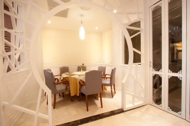 A private dining room with a round table set with a yellow cloth and grey upholstered chairs, seen through a white circular lattice archway.