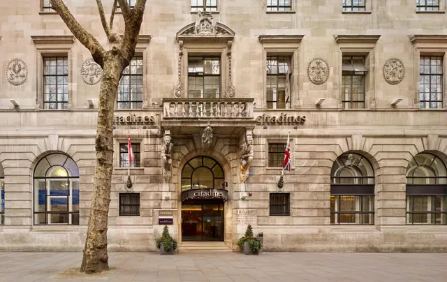 The stone facade of a Citadines hotel building with arched windows, an entrance canopy and a tree on the pavement in front.