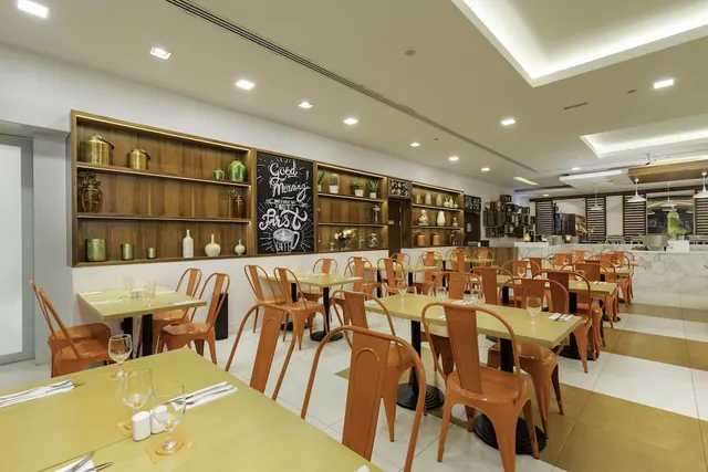 A restaurant dining room with yellow tables, orange chairs, wooden display shelves and a chalkboard sign reading Good Morning, with a buffet counter in the background.