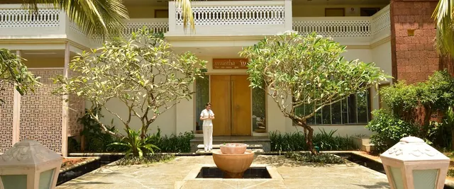 A landscaped courtyard with a central fountain leads to a building entrance with decorative balconies.