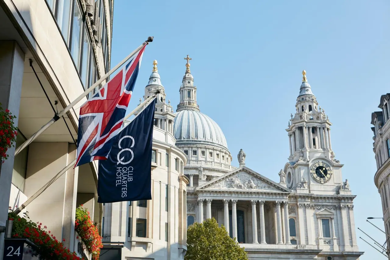 A Union Jack and a navy Club Quarters Hotel flag hang from the facade of a building, with St Paul's Cathedral visible behind.