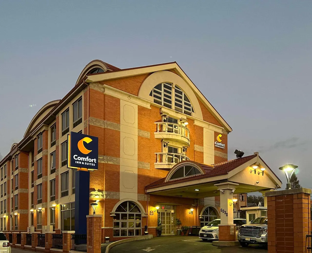 Exterior of a Comfort Inn & Suites building at dusk, with illuminated signage, a covered front entrance and parked cars.