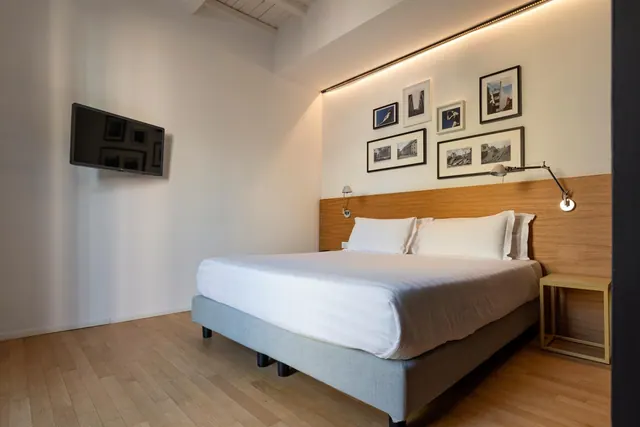 A bedroom with a made king-size bed, a wall-mounted television and framed black-and-white prints above the headboard.