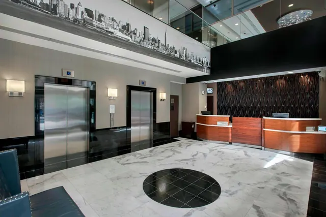 A hotel lobby with two elevators, a reception desk, a large black-and-white skyline mural and a marble floor with a black circular inlay.