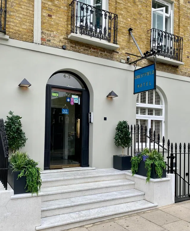 The front of the Crestfield Hotel, showing an arched dark entrance door, marble steps, potted plants and a hanging blue sign.