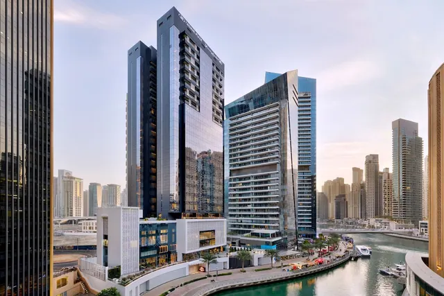 Elevated view over a canal lined with high-rise towers, with boats moored along the water and a palm-lined promenade below.