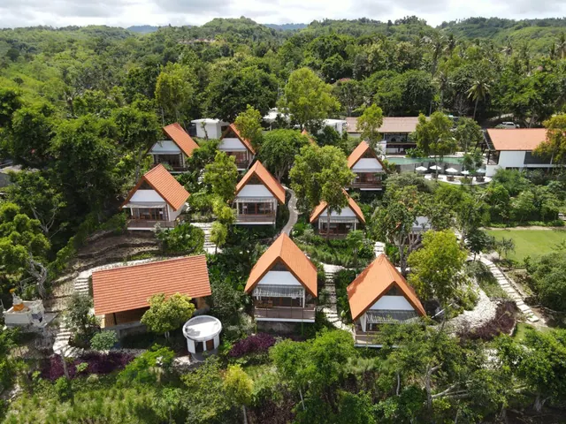 Aerial view of a cluster of orange-roofed bungalows set among dense green trees, with a small pool, loungers and a lawn visible at the upper right.