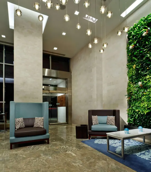A lobby with pendant lights above two armchairs, a coffee table on a blue rug, a living plant wall and a lift in the background.