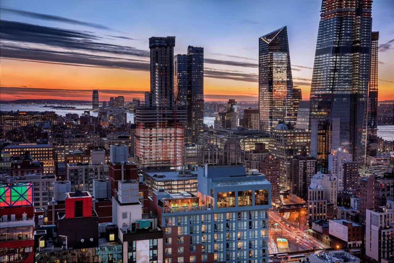 Elevated sunset view over Manhattan rooftops and the Hudson Yards towers, with the Hudson River visible at left.