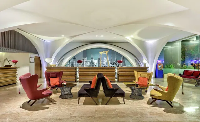 The lobby has an arched white ceiling, a wooden reception counter with a black and white city skyline mural behind it, and groups of armchairs and low tables on a stone floor.