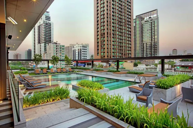 A rooftop swimming pool with loungers and planters, with high-rise buildings visible behind it at dusk.