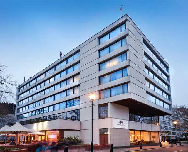 The exterior of a multi-storey hotel building with a DoubleTree sign at dusk, with lit windows, canopy umbrellas over outdoor seating and a street lamp in front.